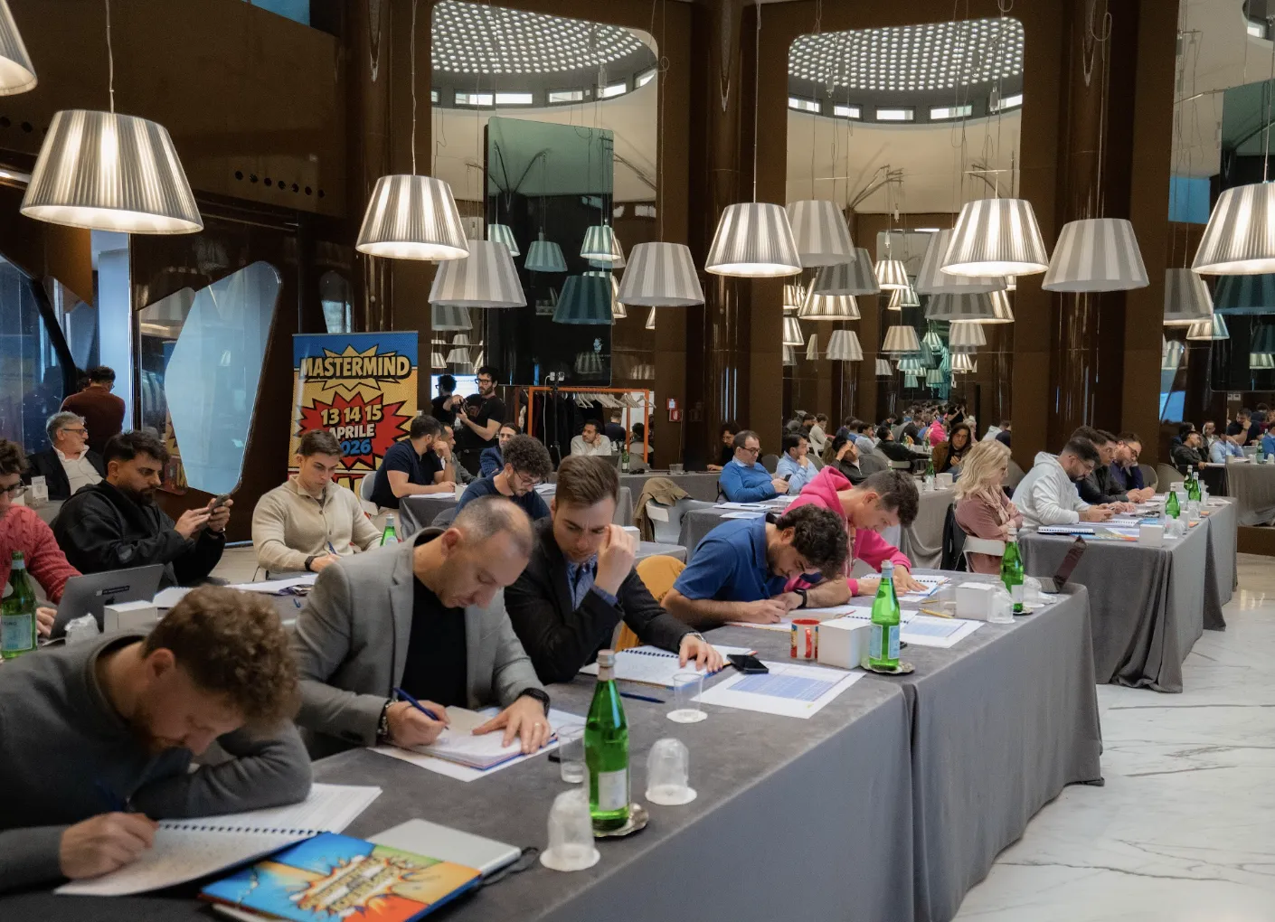 I partecipanti al Mastermind al lavoro ai tavoli della sala, con il banner dell’edizione 13-15 aprile alle spalle